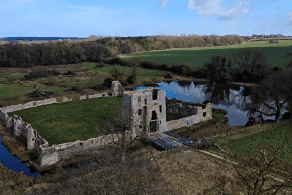 Aerial view of Baconsthorpe Castle ruins surrounded by moat, lake, and countryside in Norfolk, England