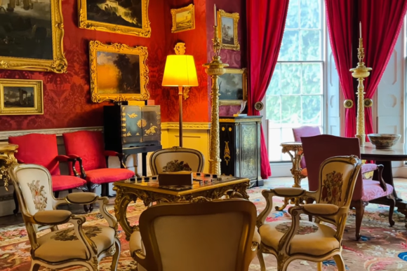 Richly decorated interior room at Felbrigg Hall with red walls, gilded furniture, framed paintings, and upholstered chairs arranged around ornate tables.