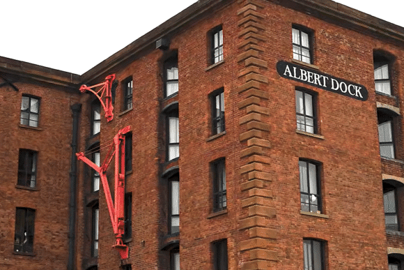 Brick warehouse building at Royal Albert Dock Liverpool with a sign reading “Albert Dock” and a red crane arm fixed to the wall.