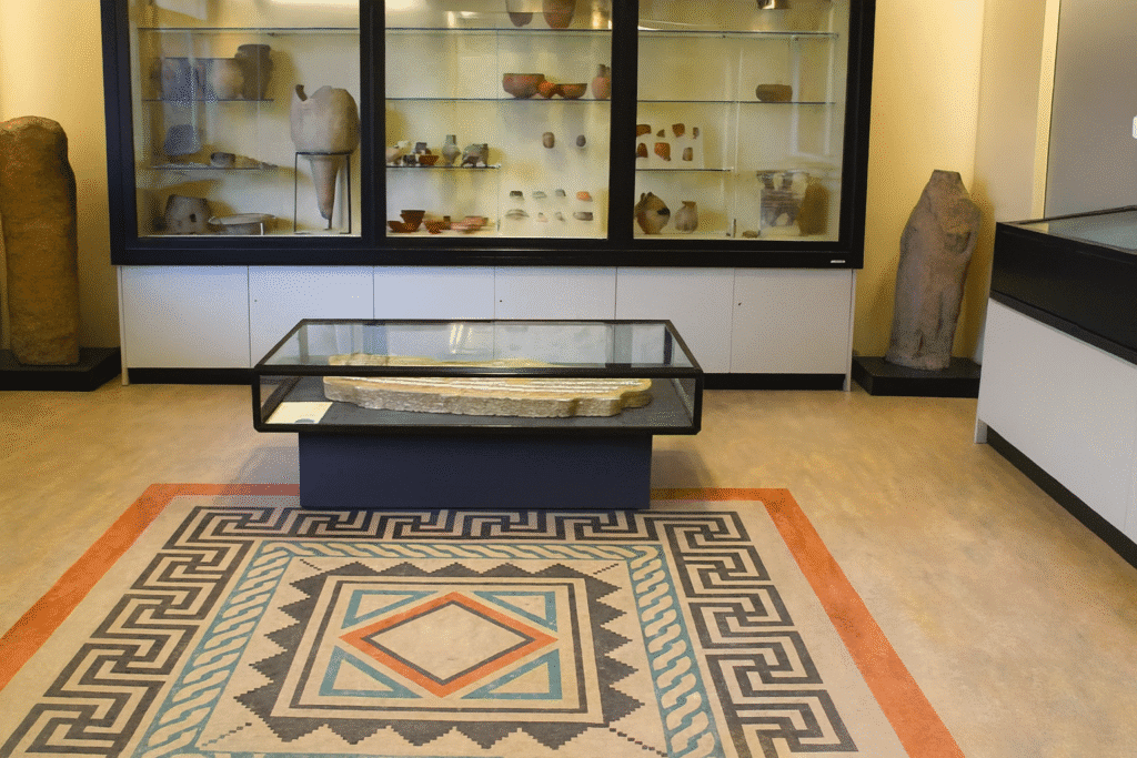 Museum display room showing Roman artefacts in glass cases and a decorative Roman-style mosaic floor.