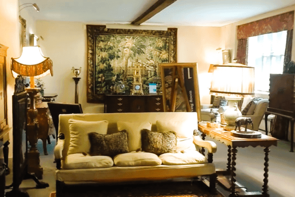 Historic living room at Anglesey Abbey featuring antique furniture, tapestry wall art, lamps, and a cream upholstered sofa.