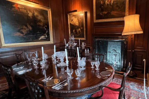 Elegant historic dining room at Antony House in Cornwall with wood-panelled walls, antique furniture, silverware, and classical paintings.