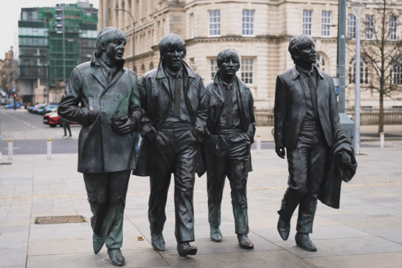 Bronze statues of four figures walking together on Liverpool’s waterfront, with city buildings in the background.