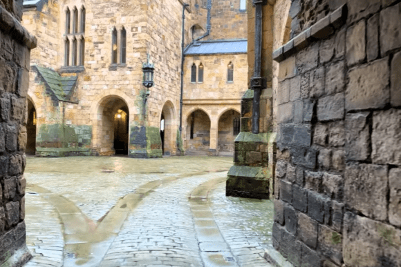 View of the inner courtyard at Alnwick Castle, showing stone walls, arches, cobblestone paving, and historic architectural details.