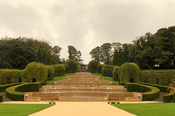 The Grand Cascade water feature at Alnwick Garden with tiered fountains, manicured hedges, and landscaped greenery.