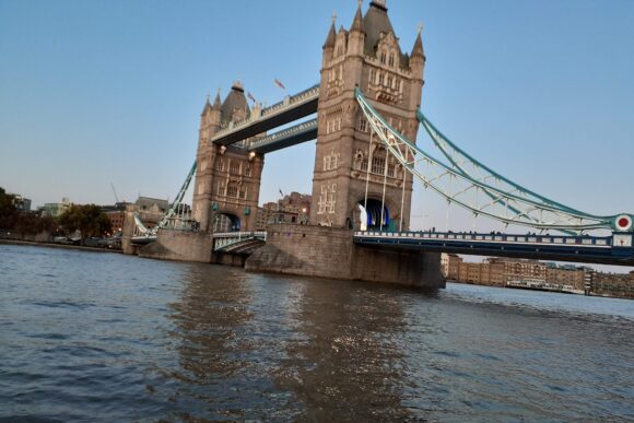 Tower Bridge in London spanning the River Thames at dusk, featuring illuminated Gothic towers and blue suspension walkways.
