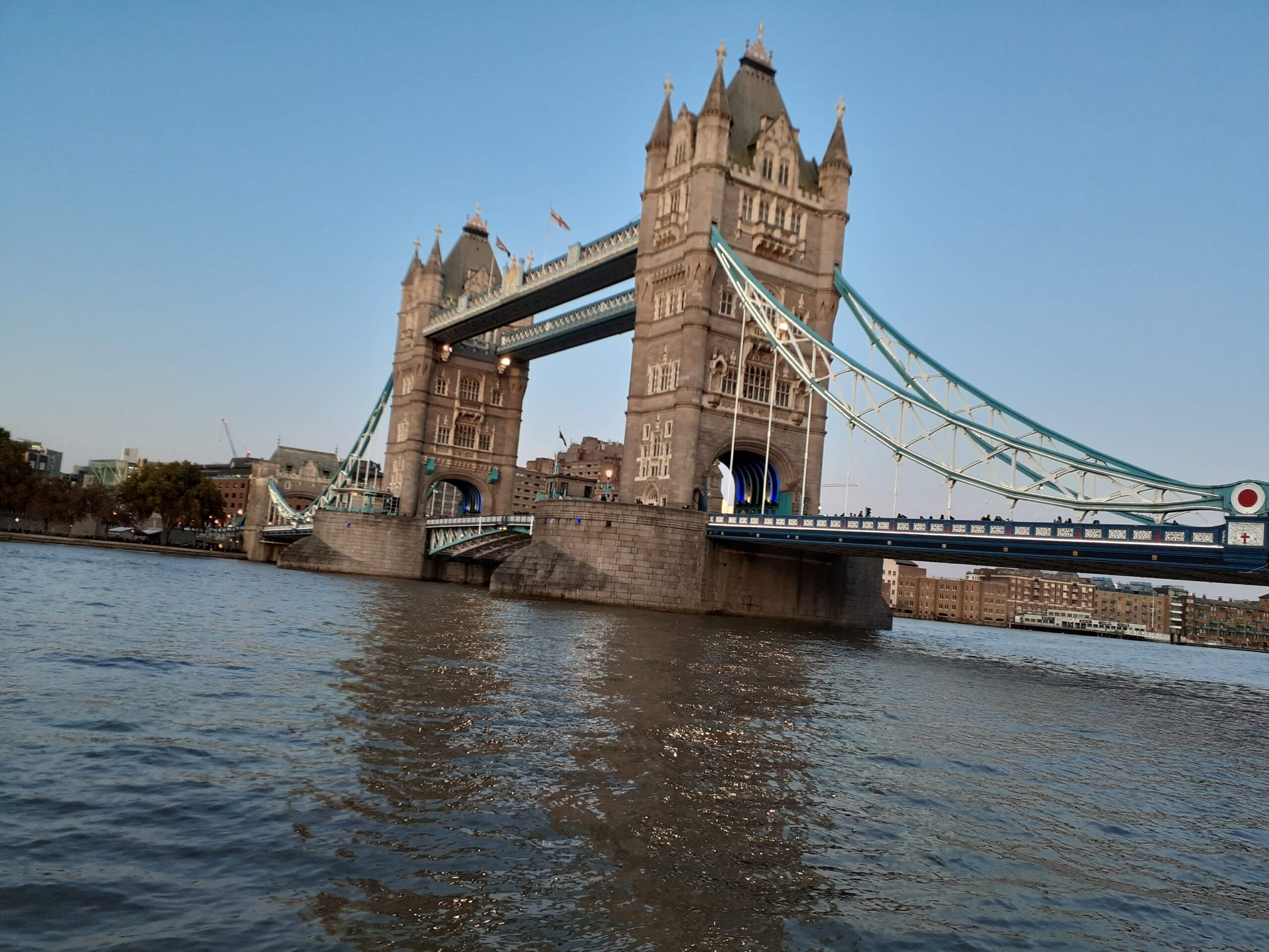 Tower Bridge in London spanning the River Thames at dusk, featuring illuminated Gothic towers and blue suspension walkways.