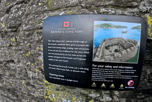 English Heritage information sign for Bayard’s Cove Fort mounted on the stone wall in Dartmouth, Devon