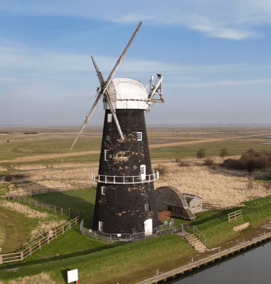 Historic Berney Arms Windmill standing beside the river on the Norfolk marshes with sails and black brick tower.