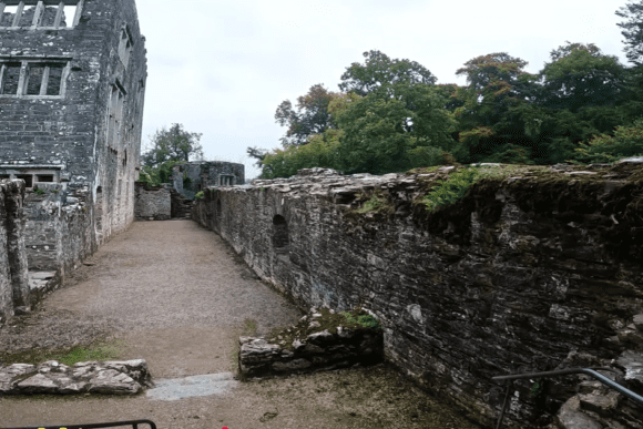 Pathway between moss-covered stone walls and medieval ruins at Berry Pomeroy Castle in Devon.