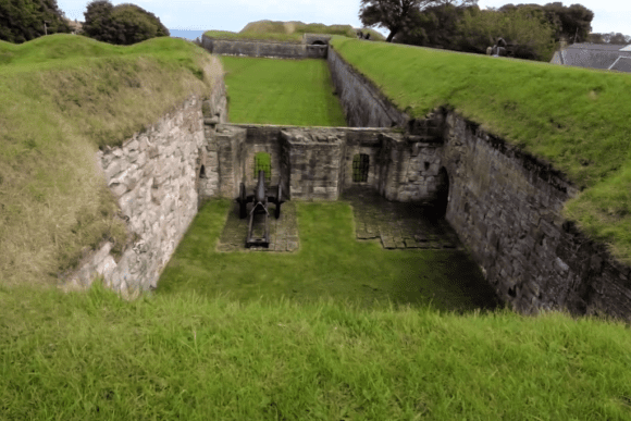 A sunken artillery position within the Berwick-upon-Tweed ramparts, featuring stone walls, grassy banks, and an old cannon.