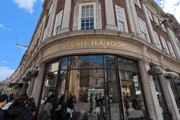 Historic Bettys Café Tea Rooms building in York with its elegant curved corner façade, large windows and visitors queuing outside the famous Yorkshire tea room.