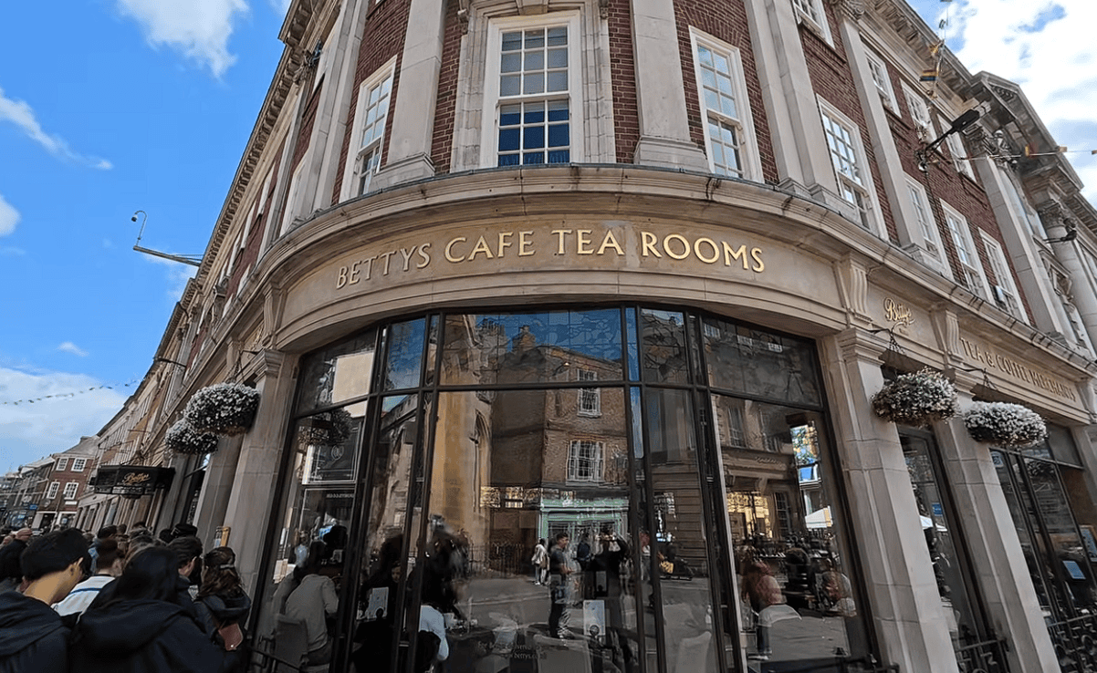 Historic Bettys Café Tea Rooms building in York with its elegant curved corner façade, large windows and visitors queuing outside the famous Yorkshire tea room.