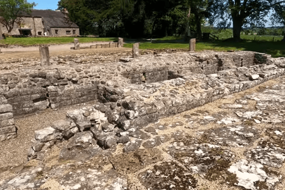Stone barracks foundations at Birdoswald Roman Fort on Hadrian’s Wall, Cumbria, surrounded by trees and grass.