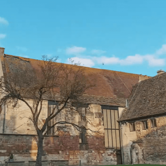 Medieval exterior of Blackfriars Priory in Gloucester with stone walls and timber roof under blue sky