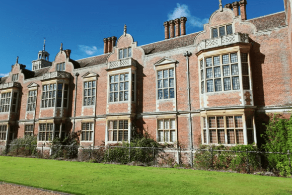 Historic red-brick Jacobean mansion façade with tall chimneys and mullioned windows at Blickling Estate, Norfolk, viewed beside formal lawns