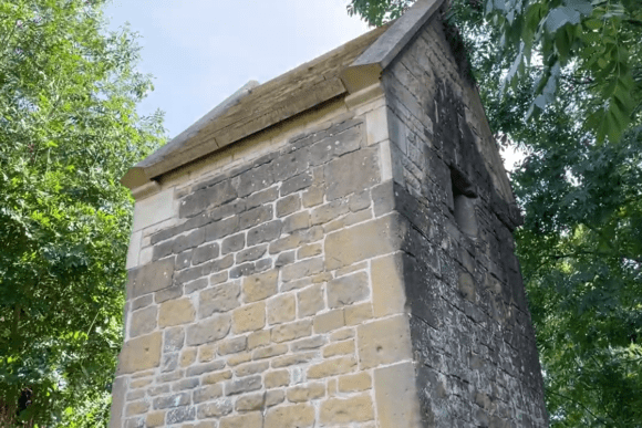 Stone-built historic Cundy House at Bolsover, surrounded by trees, showing a pitched roof, weathered masonry, and corner buttress detailing.