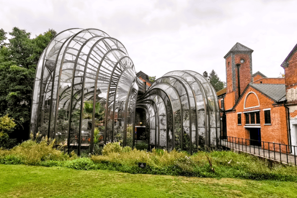Glasshouses at the Bombay Sapphire Distillery in Hampshire surrounded by landscaped gardens and historic red-brick mill buildings.