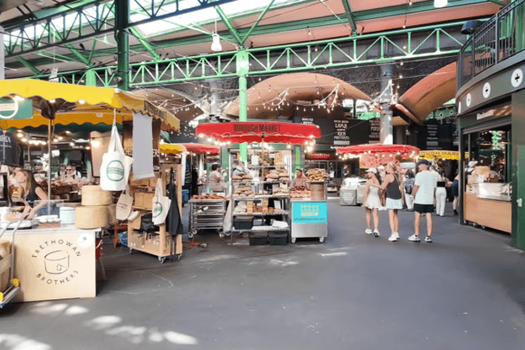 Busy interior of Borough Market in London with artisan food stalls, fresh bread displays, colorful market canopies, and visitors exploring the historic covered marketplace.