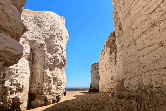 White chalk cliffs and towering sea stacks at Botany Bay in Broadstairs, Kent, framing a sandy beach with views of the North Sea under a clear blue sky.