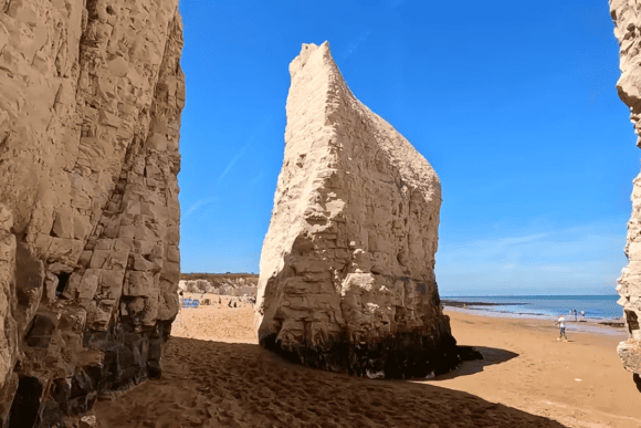 Towering white chalk sea stack at Botany Bay in Broadstairs, Kent, surrounded by golden sand and the North Sea beneath a clear blue sky.