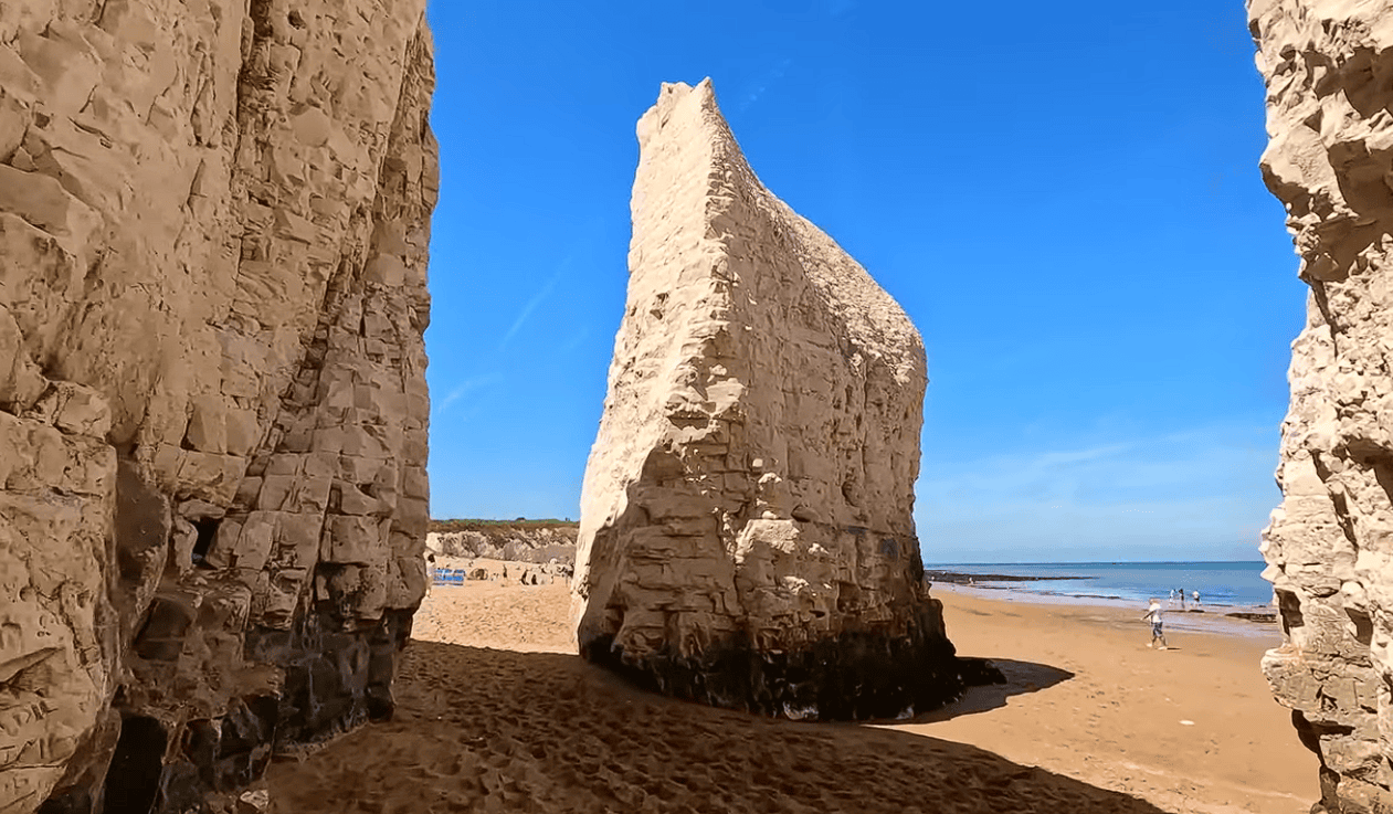 Towering white chalk sea stack at Botany Bay in Broadstairs, Kent, surrounded by golden sand and the North Sea beneath a clear blue sky.