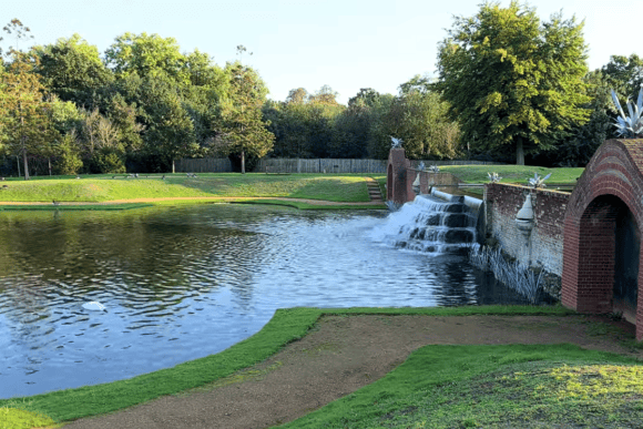 Diana Fountain in Bushy Park, London, featuring cascading waterfalls, ornamental brickwork, and a tranquil pond surrounded by lush trees and landscaped gardens.