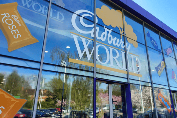 Exterior entrance to Cadbury World in Birmingham featuring the large Cadbury World logo and colourful Cadbury chocolate branding on the glass façade.