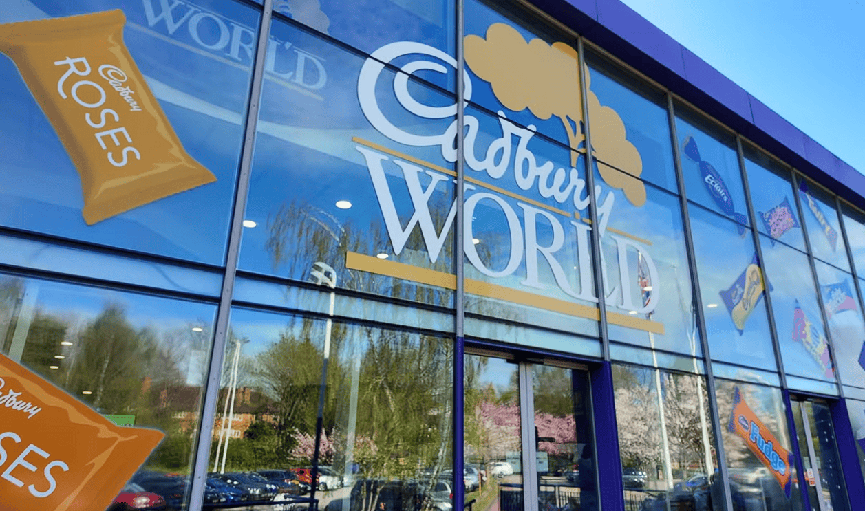 Exterior entrance to Cadbury World in Birmingham featuring the large Cadbury World logo and colourful Cadbury chocolate branding on the glass façade.