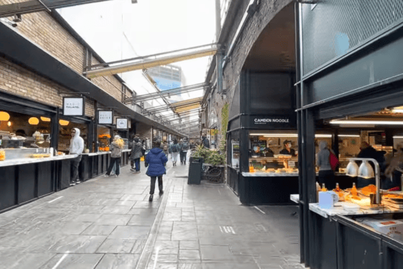 Food stalls inside Camden Market in London, with visitors exploring a covered walkway lined with international street food vendors and eateries.