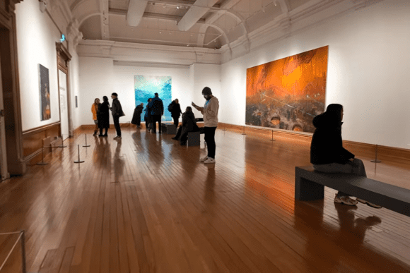 Visitors viewing large contemporary paintings inside Cartwright Hall Art Gallery, with spacious exhibition rooms, polished wooden floors, and modern artworks displayed in a historic gallery setting.