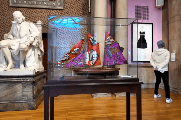 Eclectic art display at Cartwright Hall Art Gallery featuring a colourful model sailing ship in a glass case, historic marble sculpture, contemporary artwork, and visitors exploring the gallery in Bradford.