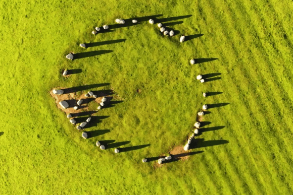 Aerial view of Castlerigg Stone Circle showing a near-complete ring of standing stones casting long shadows across bright green grass.