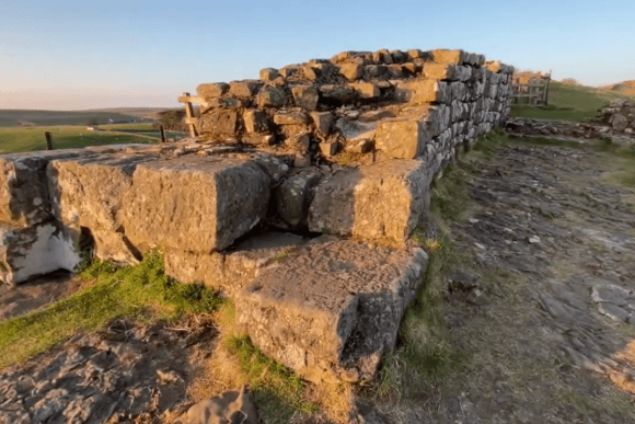 Close-up of weathered stone blocks forming Cawfields Roman Wall, part of Hadrian’s Wall, lit by warm evening light with open countryside beyond.