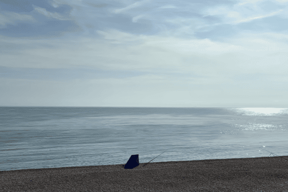 Calm morning view of Chesil Beach at the Portland end, with a peaceful shingle shoreline, sparkling sea, and anglers fishing along the famous Dorset Jurassic Coast.
