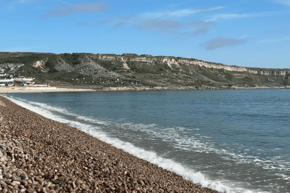 Pebble shoreline at Chesil Beach near Portland with gentle waves, dramatic limestone cliffs, and clear blue waters along Dorset’s UNESCO Jurassic Coast.