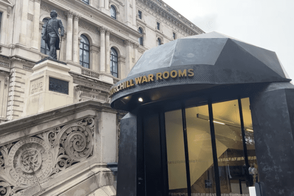 Entrance to Churchill War Rooms with modern canopy beside historic government buildings in London.