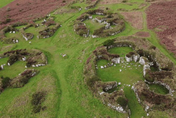Aerial view of Chysauster Ancient Village showing circular stone house remains set in open countryside.