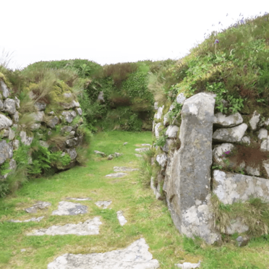 Stone entrance passage at Chysauster Ancient Village with grass path and moss-covered granite walls.