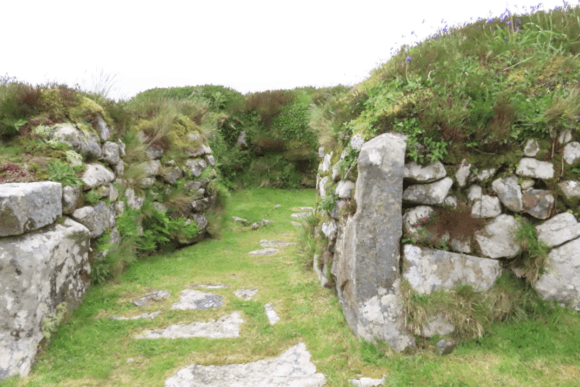 Stone entrance passage at Chysauster Ancient Village with grass path and moss-covered granite walls.