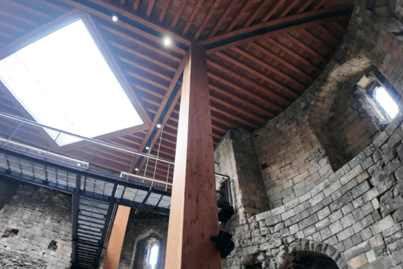 Interior of Clifford's Tower in York showing stone walls, timber roof, and modern walkway.