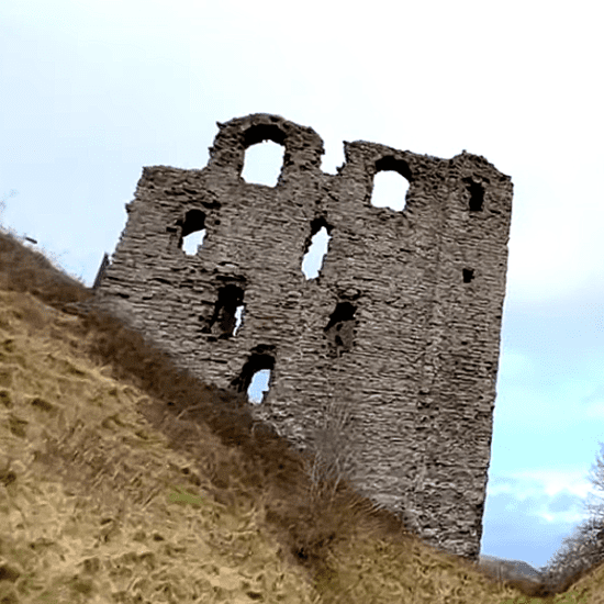 Ruined stone keep of Clun Castle standing on a grassy hillside.