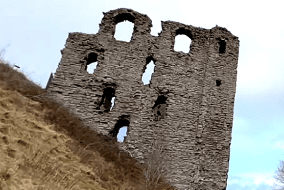 Ruined stone keep of Clun Castle standing on a grassy hillside.