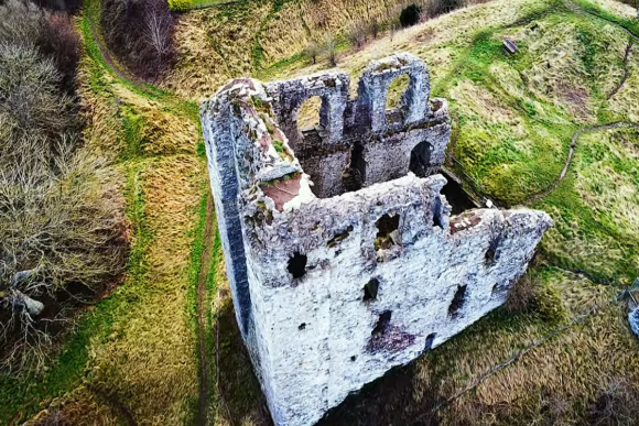 Aerial view of the ruined stone keep of Clun Castle, showing collapsed walls and arched window openings on a grassy hillside.