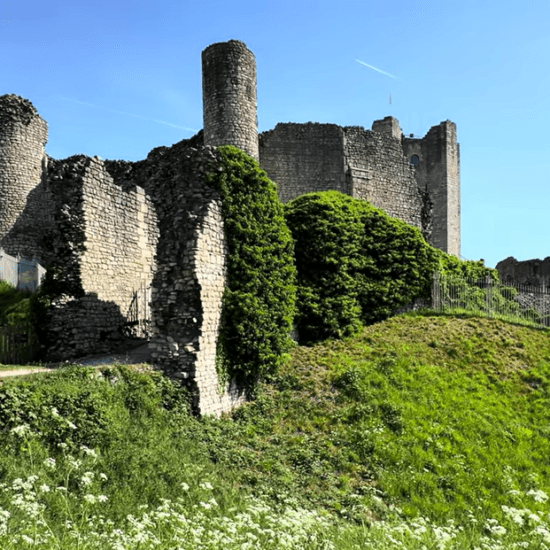 Stone ruins of Conisbrough Castle on a grassy hill, with the round keep rising above the outer walls.