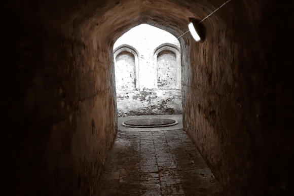 Stone tunnel inside Coombe Conduit leading to an arched opening with historic water chambers beyond.
