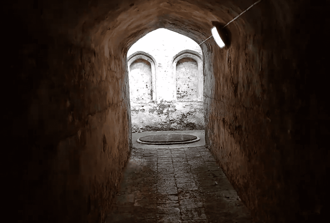 Stone tunnel inside Coombe Conduit leading to an arched opening with historic water chambers beyond.