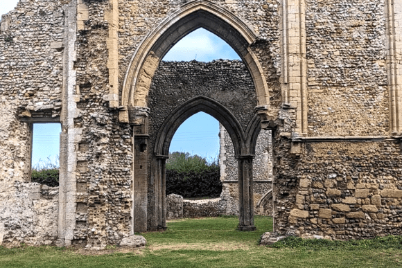 Stone archway and flint walls of Creake Abbey ruins opening onto a grassy courtyard.