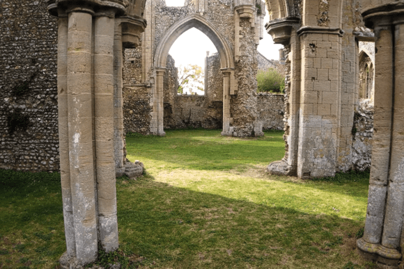 Stone columns and pointed arches inside the ruins of Creake Abbey, opening onto a grassy interior.