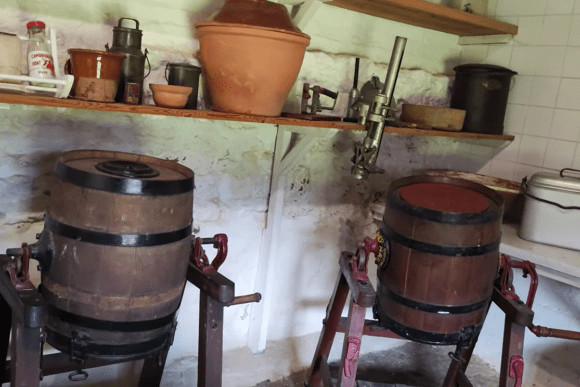 Historic dairy room at Denny Abbey & Farmland Museum with two wooden barrel churns and shelves of traditional containers.